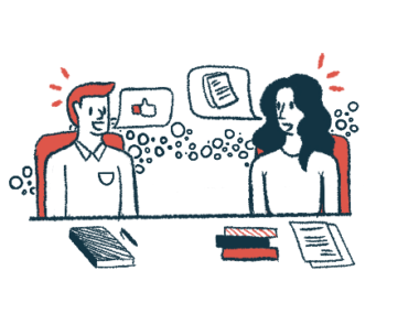 Two people are seen talking to each other during a meeting, with notebooks and papers on the table in front of them.