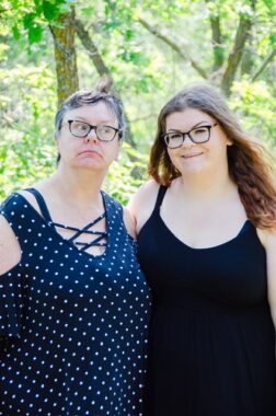 Two women — mother and daughter — stand embracing in a forested area.
