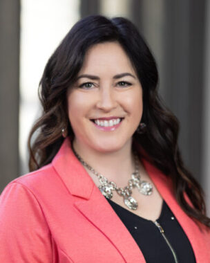A headshot shows a woman with long, dark hair wearing a pink blazer over a black shirt.