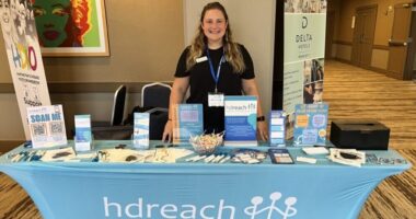 A woman stands behind a booth with HD Reach on it.