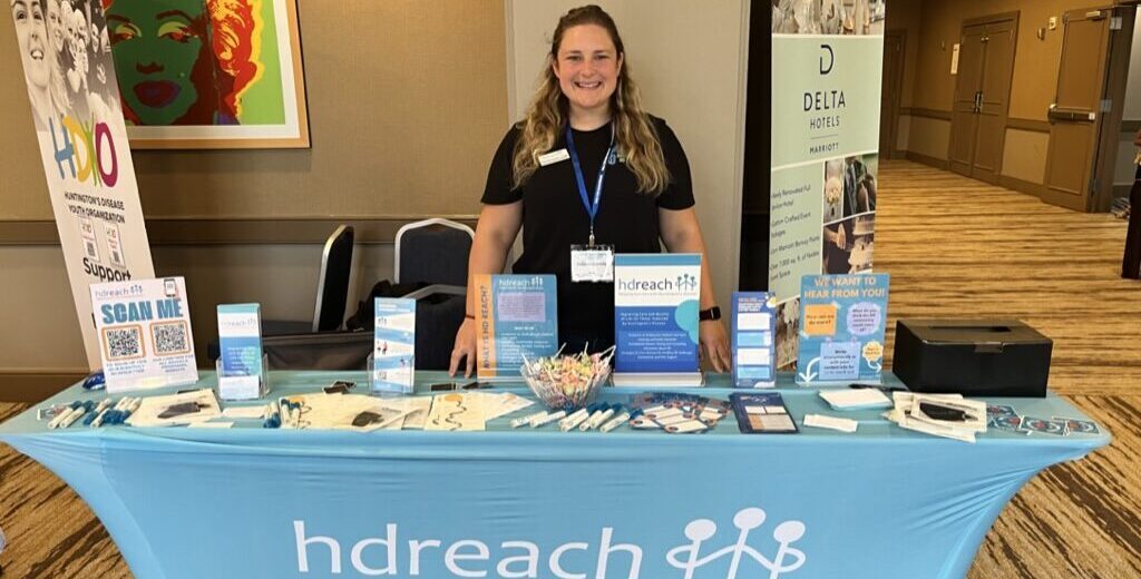 A woman stands behind a booth with HD Reach on it.