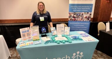 A woman stands at a table filled with Huntington's disease information.